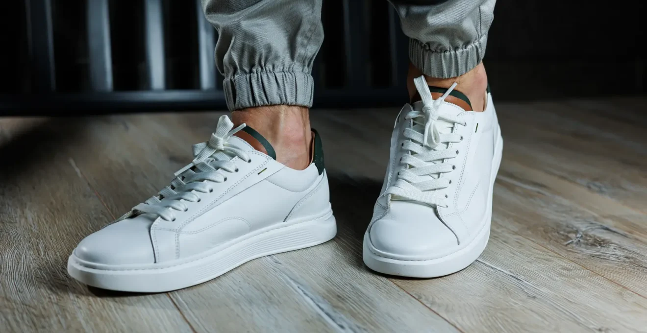 Un homme attache les lacets de ses baskets montantes en cuir blanc sur un trottoir parisien