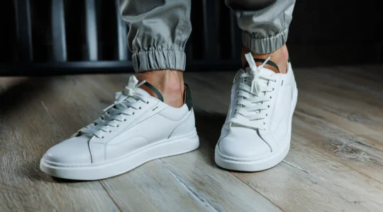 Un homme attache les lacets de ses baskets montantes en cuir blanc sur un trottoir parisien