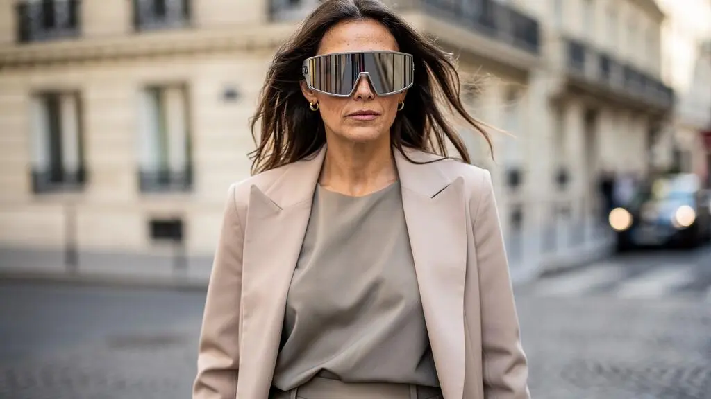 Une femme porte des lunettes de soleil masque en marchant dans une rue parisienne.